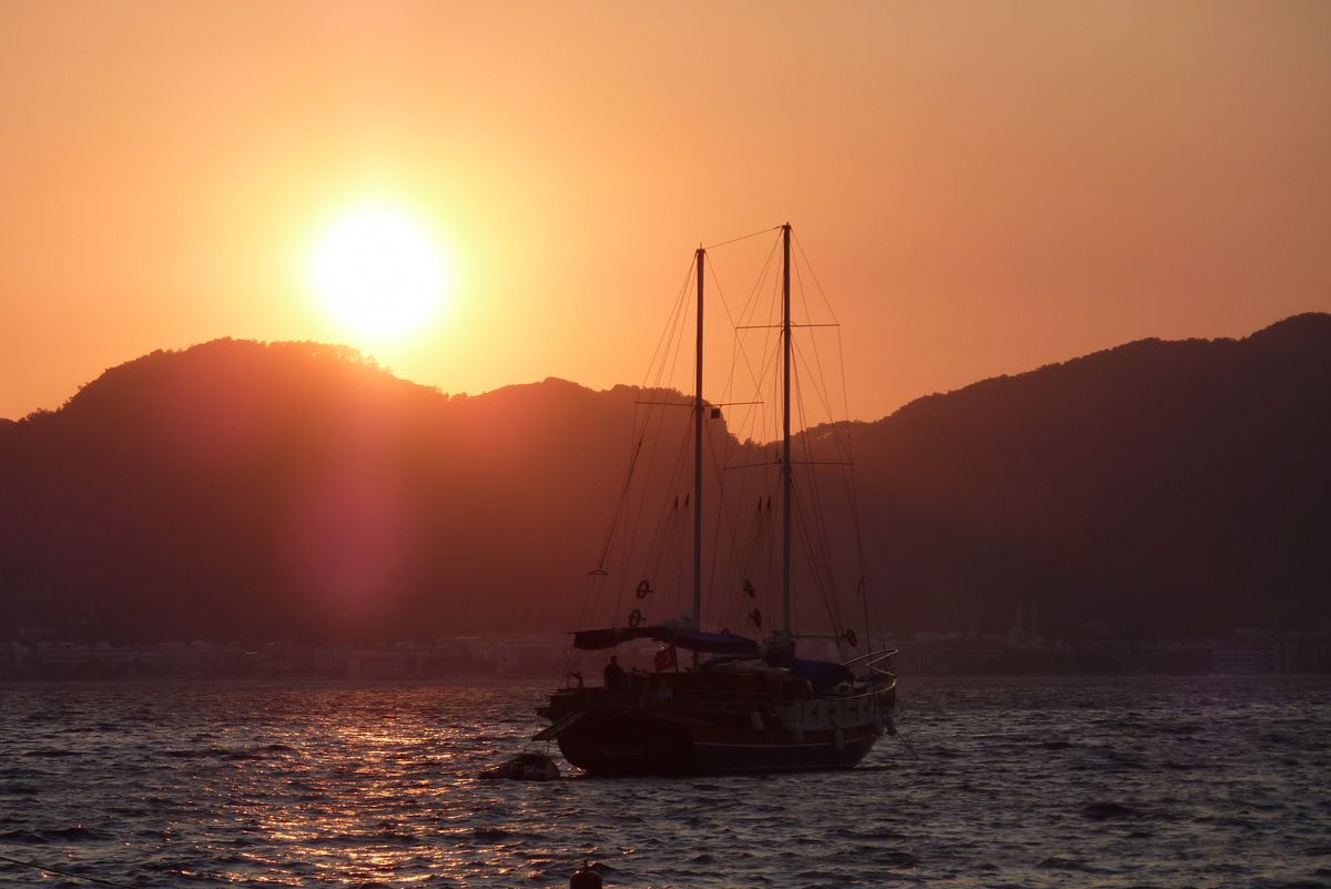 Een sfeerbeeld van de ondergaande zon met op de voorgrond een schip.