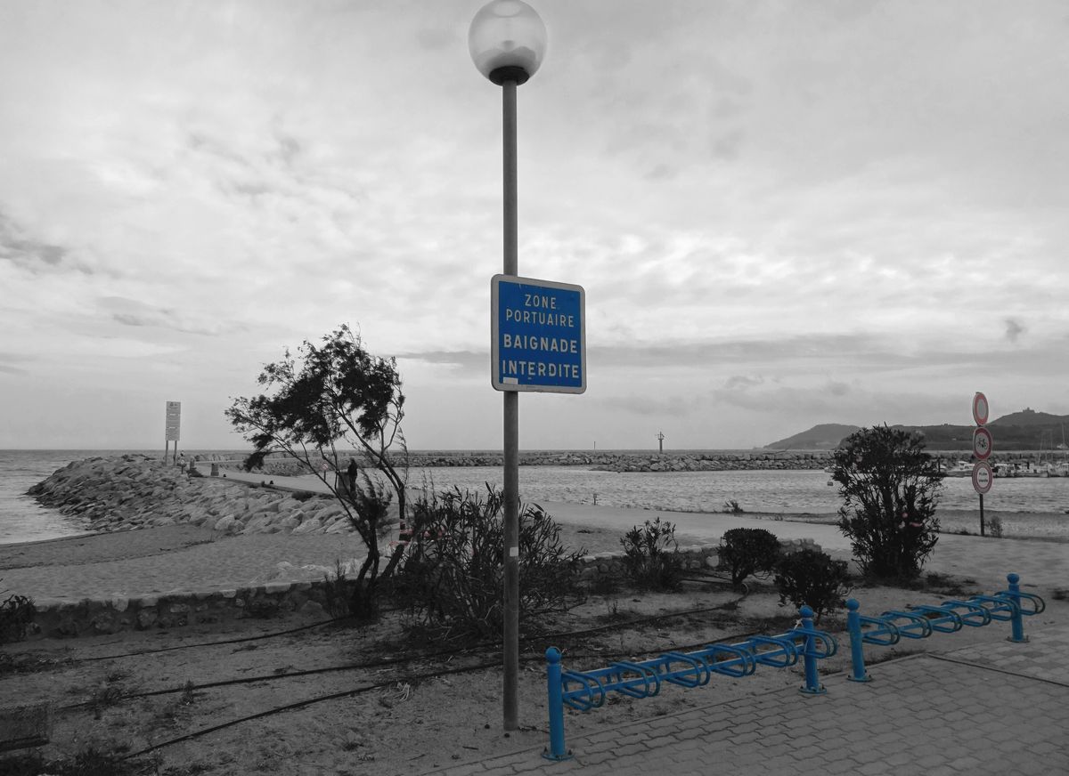 Un lampadaire, un parking à vélos, une digue, des panneaux, la côte. Des bleus, des blancs, des gris, du rouge et du noir